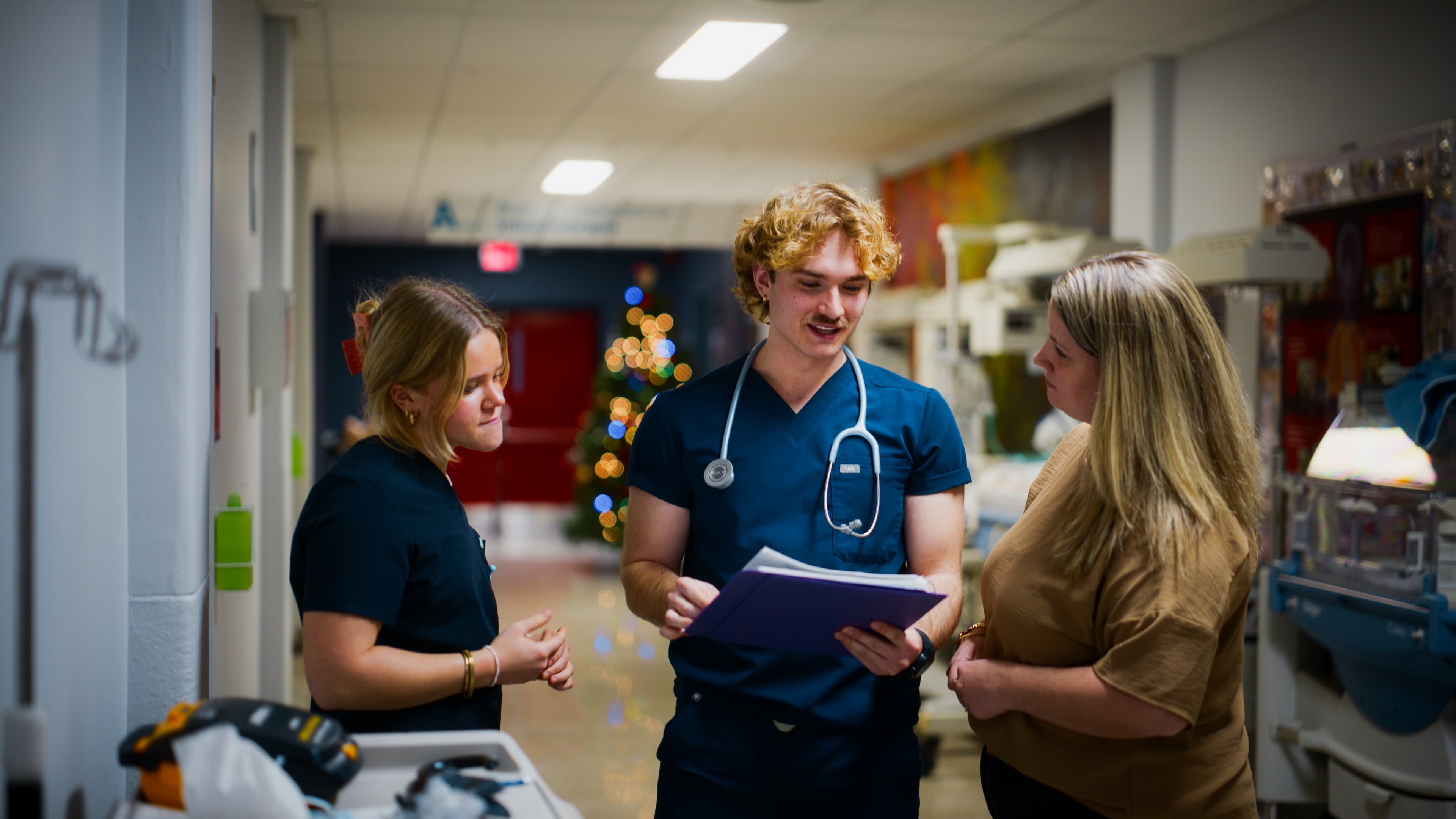Three healthcare professionals reviewing a file in a care unit corridor